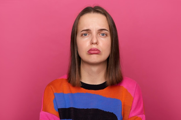 Image d'une triste femme stressée déprimée portant un pull coloré posant isolé sur fond rose regardant la caméra avec des lèvres boudeuses étant de mauvaise humeur exprimant des émotions négatives