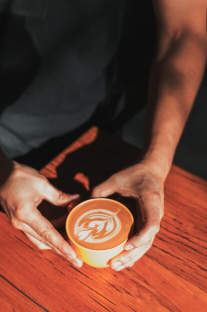 Image verticale du serveur mâle adulte brunet montrant du café dans une tasse jaune