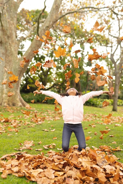 Image verticale d'une heureuse fille afro-américaine s'amusant avec des feuilles dans le jardin