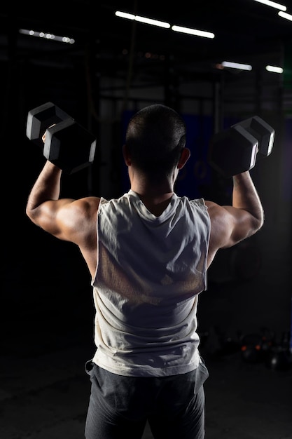 Image verticale d'un homme musclé du dos en appuyant avec une paire d'haltères