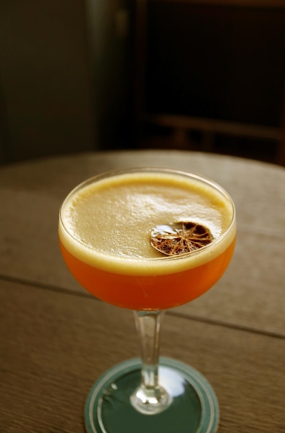 Image verticale d'un verre de cocktail orange sur la table ronde en bois