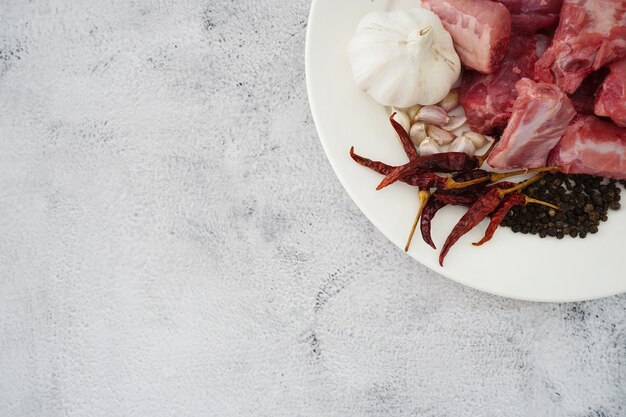 Image de viande crue poivre à l'ail et piments séchés dans une assiette blanche sur fond blanc