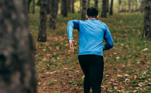 Image vue arrière d'un coureur qui court en plein air dans le fond de la forêt Homme de remise en forme faisant de l'exercice dans le parc portant des vêtements de sport bleus et noirs Concept de personnes et de sport