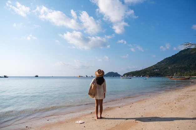 Image vue arrière d'une femme avec chapeau et sac se promener sur la plage avec fond de ciel bleu