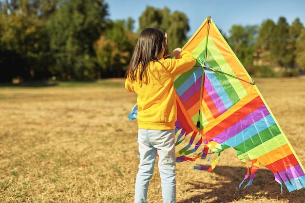 Image vue arrière d'une petite fille heureuse qui lance un cerf-volant coloré par une journée ensoleillée à l'extérieur