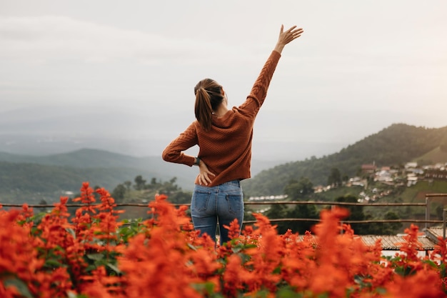 Image de la vue arrière d'une voyageuse assise et regardant un magnifique champ de fleurs de montagne et une vue sur la naturexA