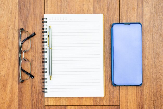 Image vue de dessus du cahier ouvert avec des pages vierges et téléphone portable, oeil glasse sur fond de table en bois pour ajouter du texte ou une maquette