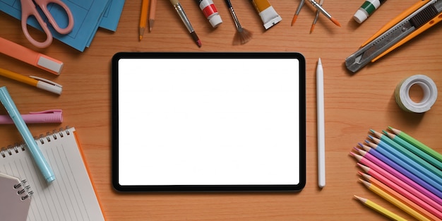 L'image vue de dessus de l'espace de travail de l'artiste est entourée d'une tablette informatique à écran blanc et d'autres choses.