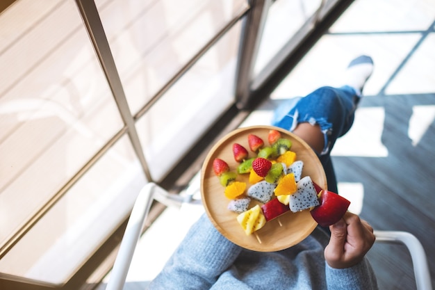 Image vue de dessus d'une femme tenant une assiette en bois de fruits frais mélangés sur des brochettes