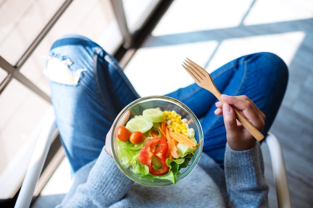 Image vue de dessus d'une femme tenant un bol de salade de légumes frais tout en étant assise sur une chaise