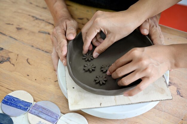 Image de la vue de dessus Mains faisant une poterie en argile décorant une plaque d'argile sur une table de travail