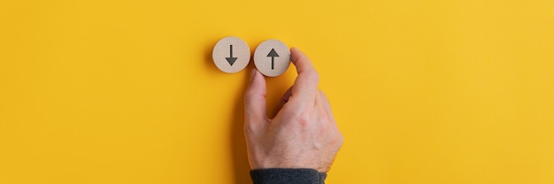 Image de vue large de la main masculine plaçant deux cercles coupés en bois avec des flèches pointant vers le haut et vers le bas sur le jaune.