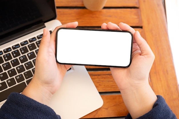 Une image en vue supérieure d'une femme tenant une maquette de smartphone à écran blanc dans une position horizontale