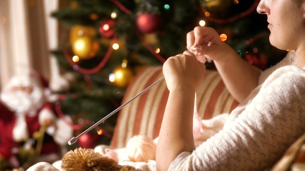 Images 4K d'une belle jeune femme assise dans un fauteuil à côté d'un sapin de Noël décoré et de chaussettes en laine tricotées. Les gens se détendent pendant les vacances d'hiver et les célébrations à la maison