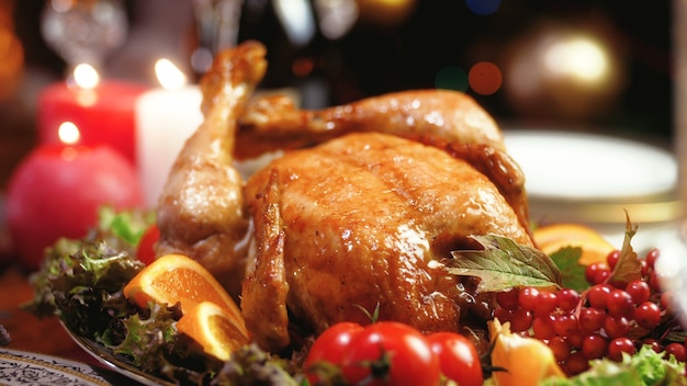 Images de gros plan 4k de poulet fraîchement cuit, de bougies allumées et de lumières de Noël rougeoyantes sur une table en bois dans le salon. Table à manger servie pour la grande famille pendant les vacances d'hiver et les célébrations.