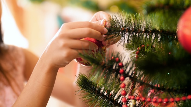 Images en gros plan de mains féminines suspendues à une boule colorée sur un arbre de Noël. Maison de décoration familiale pendant les vacances d'hiver et les fêtes.