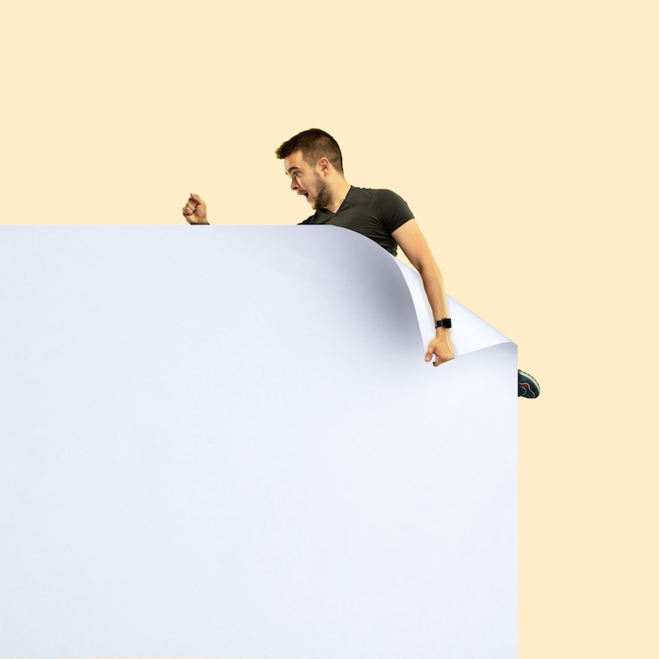 Photo imaginez qui couvre une feuille blanche pour obtenir une icône de fichier numérique. jeune homme sportif décontracté attrapant le bord d'une énorme feuille de papier. monde numérique, imagination amusante de la façon dont l'icône apparaît.