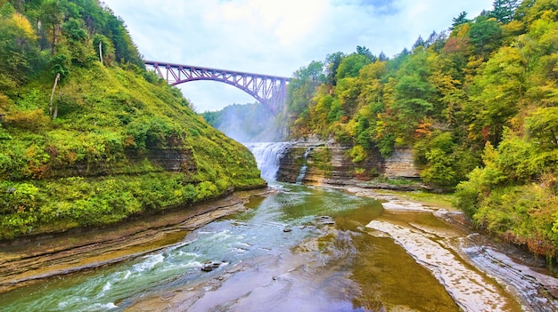 Immense canyon avec pont en arc de voie ferrée au-dessus d'une chute d'eau traversant des falaises