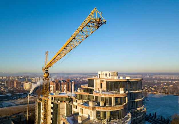 Immeuble d'appartements ou de bureaux en construction, vue de dessus. Grue à tour sur fond d'espace de copie de ciel bleu lumineux, paysage de la ville qui s'étend à l'horizon. Photographie aérienne de drone.