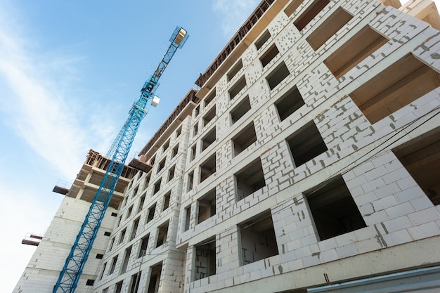 Immeuble résidentiel à plusieurs étages en construction et grue sur fond de ciel bleu