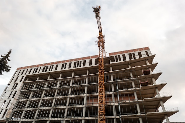 Immeuble résidentiel à plusieurs étages en construction et grue sur fond de ciel bleu