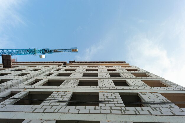 Immeuble résidentiel à plusieurs étages en construction et grue sur fond de ciel bleu