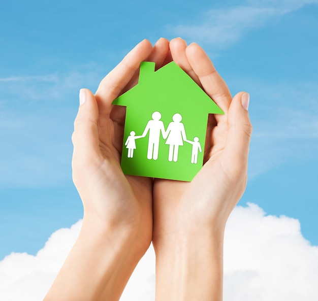 immobilier et concept de maison familiale - photo en gros plan de mains féminines tenant une maison de papier vert avec la famille