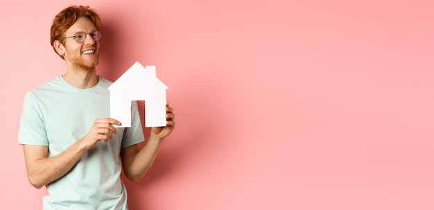 Photo immobilier homme rousse heureux rêvant d'acheter une propriété à droite et montrant la coupe de la maison en papier