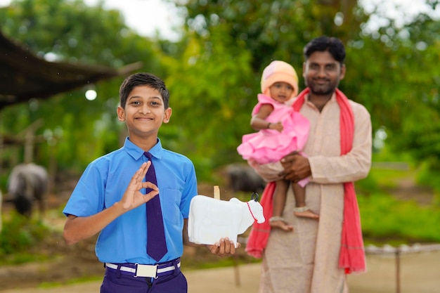 importance du concept d'épargne : petit garçon indien intelligent debout et tenant une tirelire à la main avec son père et sa petite soeur.