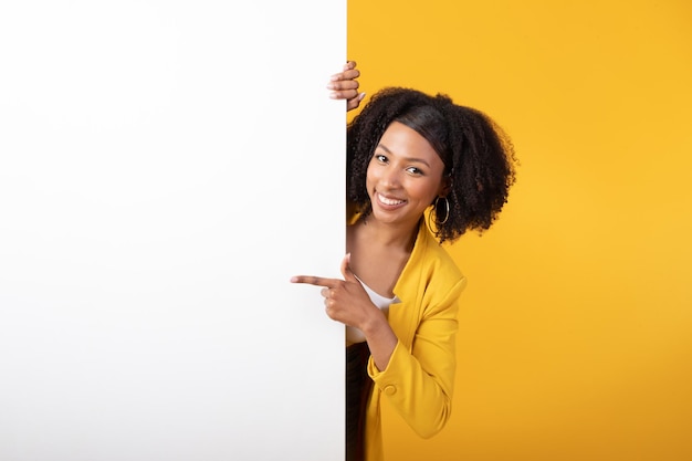 Impressionnante promo excitée dame noire pointant sur un tableau blanc avec un espace vide présentant quelque chose sur