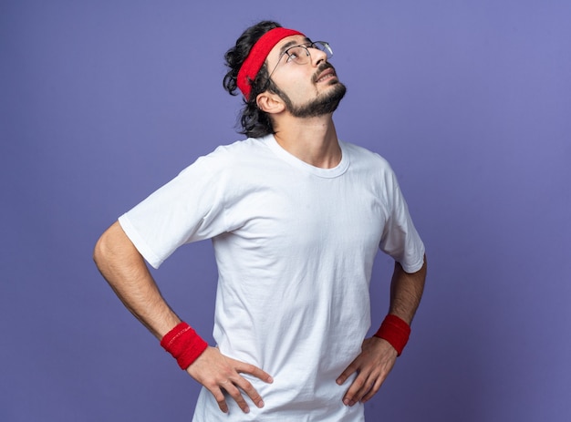 Impressionné à la recherche d'un jeune homme sportif portant un bandeau avec un bracelet mettant les mains sur la hanche