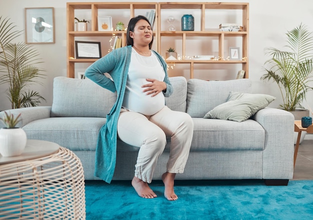 Inconfort de la femme enceinte et mal de dos assis sur le canapé du salon et tenant le ventre à la maison