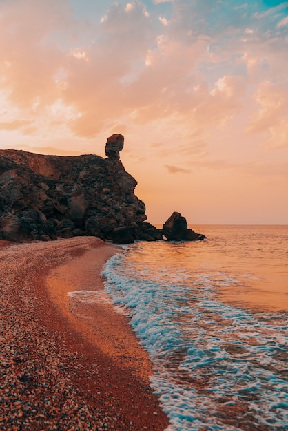 Incroyable coucher de soleil en mer, beauté de la nature. Vue panoramique sur la mer, la côte rocheuse et la plage de sable, le ciel doré et le soleil. Copiez l'espace sur le ciel fantastique. Prise de vue verticale.