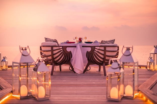 Incroyable dîner romantique sur la plage sur une terrasse en bois avec des bougies sous le ciel du coucher du soleil. Romance et amour