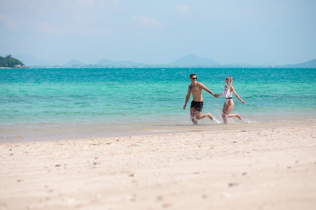 Incroyable jeune couple court sur la plage main dans la main