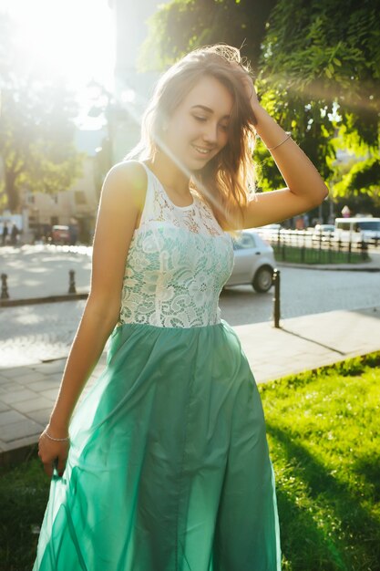 Incroyable jeune mannequin blonde avec un sourire charmant posant au lever du soleil et à l'éblouissement du soleil