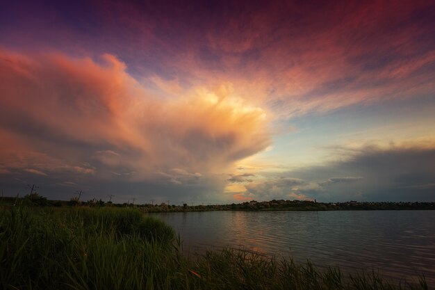 Incroyable lever de soleil au bord du lac avec des nuages colorés et de la végétation au premier plan
