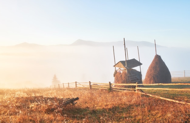 Incroyable paysage de montagne avec du brouillard et une botte de foin en automne.