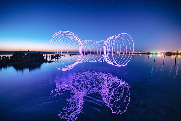 Incroyable performance de feu laser dans le ciel bleu nocturne avec des reflets dans l'eau de mer