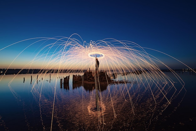 Incroyable spectacle de feu dans le ciel bleu nocturne avec des reflets dans l'eau de mer