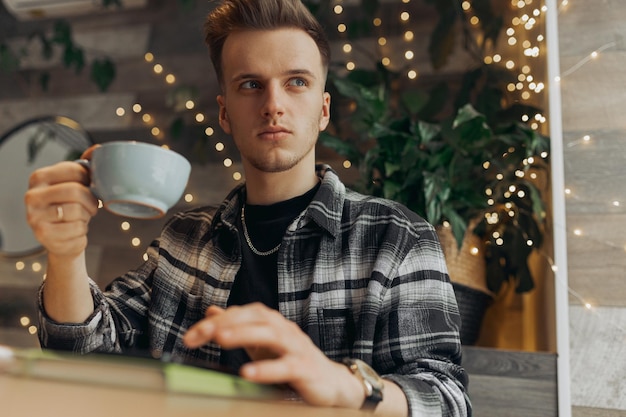 indépendant masculin pensif buvant du café et ayant une pause dans le travail à distance au café