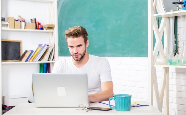 Indépendant de retour à l'école Journée de travail matin concept d'éducation moderne vie universitaire professeur d'école utiliser un ordinateur portable et un smartphone homme prendre note et boire du café étudiant homme en classe avec une tasse de thé