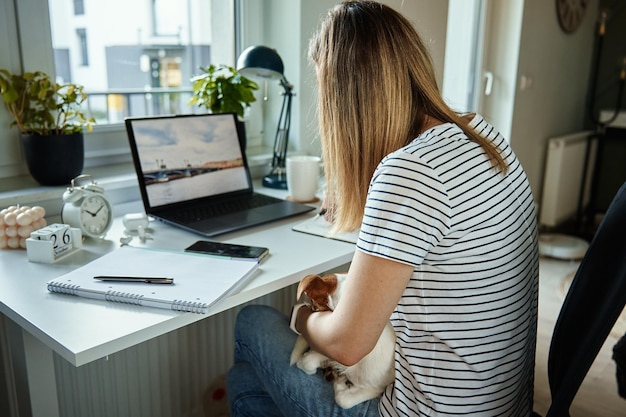 Indépendant travaillant au bureau à domicile avec un chien. Femme utilisant un ordinateur portable et écrivant dans le bloc-notes