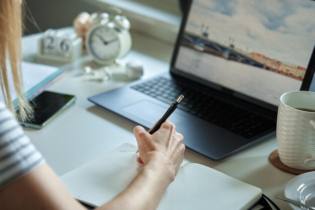 Indépendant travaillant à la maison bureau femme utilisant un ordinateur portable et écrivant dans le bloc-notes assis à table à la maison