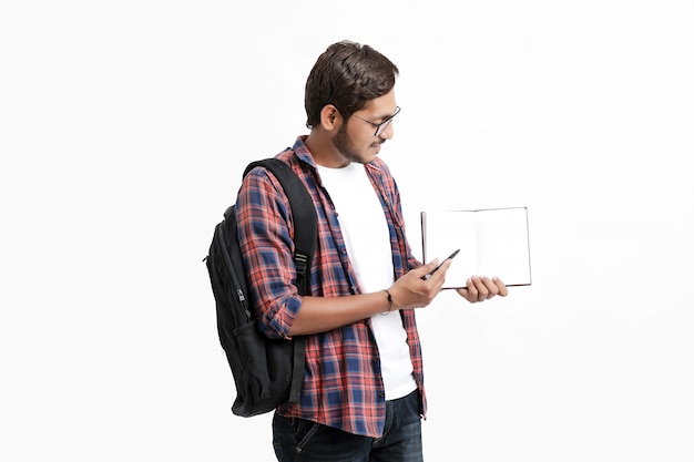 Indian college student holding cartable et montrant carnet de notes sur un mur blanc