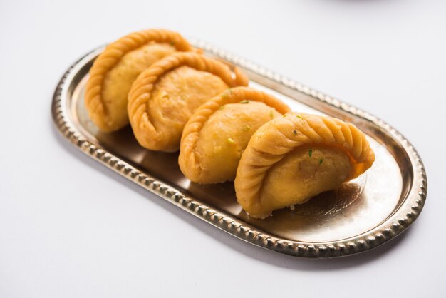 Indian Gujiya, boulettes sucrées, nourriture traditionnelle du festival Holi servie dans une plaque d'argent sur fond blanc. mise au point sélective