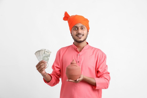 Indian man holding tirelire d'argile et monnaie en main sur mur blanc