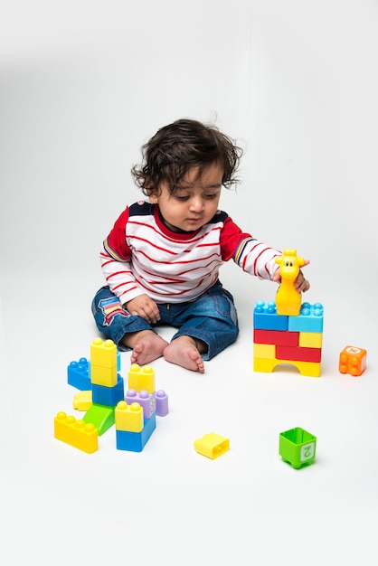 Indien mignon petit bébé ou nourrisson ou tout-petit jouant avec des jouets ou des blocs colorés sur fond blanc,