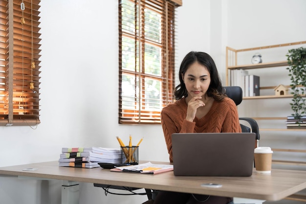 Indienne d'Asie Directrice féminine travaillant au bureau assise à un bureau analysant des statistiques commerciales tenant des diagrammes et des graphiques à l'aide d'un ordinateur portable