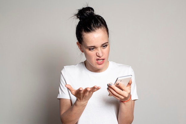 L'indignation bouleversée jeune femme regarde son smartphone voit de mauvaises nouvelles ou des photos se met en colère